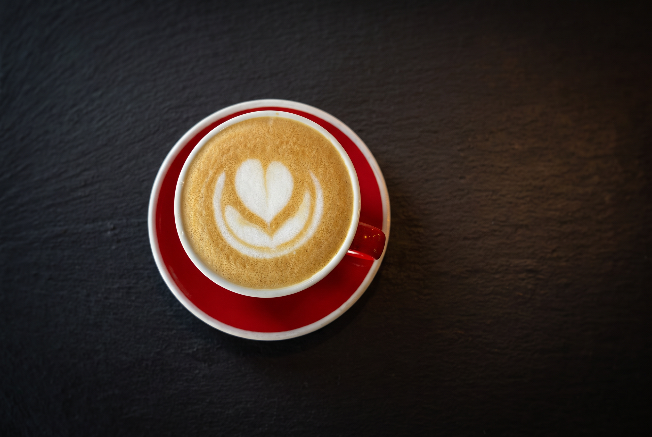 Cappuccino cu latte art în cană roșie pe fundal închis